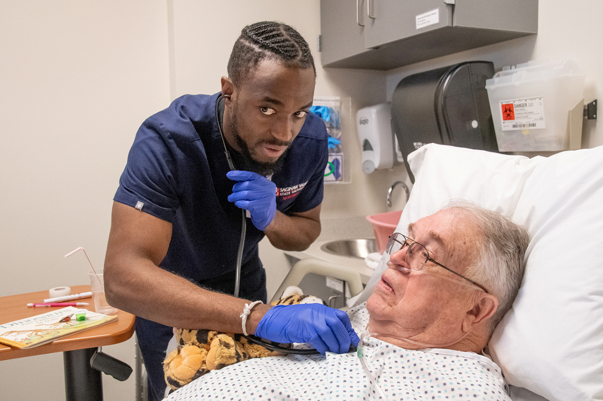 Young man in blue scrubs next to hospital bed